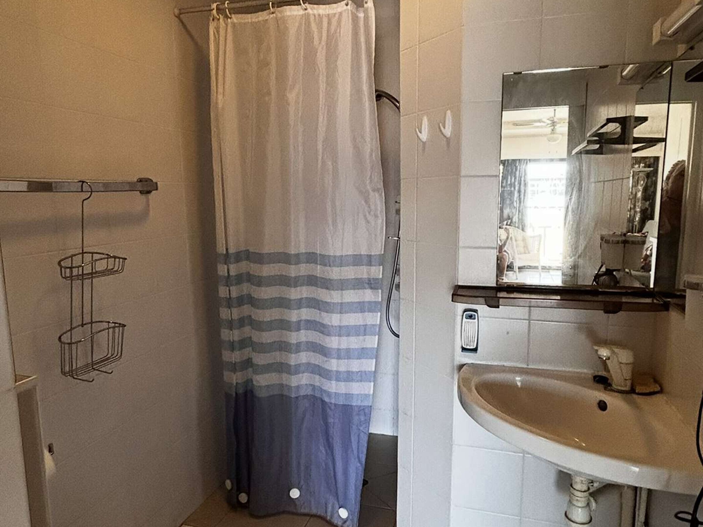 Un baño con cortina de ducha, un lavabo, un espejo y un perchero para toallas.