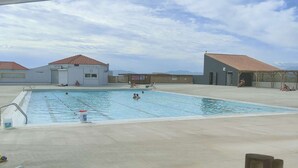 Ein Schwimmbecken mit Holzterrasse, zwei Gebäude mit roten Ziegeldächern und bewölkter Himmel.