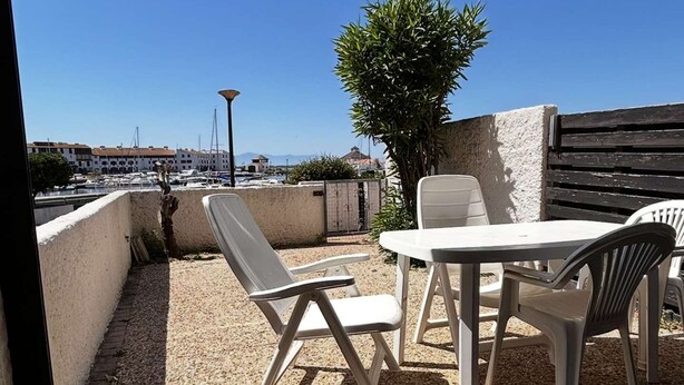 Eine Terrasse im Freien mit Tisch und Stühlen, einer Lampe und Blick auf eine Marina mit Booten.
