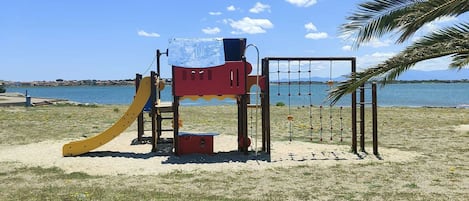 A playground with a slide and climbing structures near a beach with a clear sky.