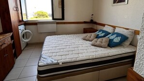 Ein Schlafzimmer mit Bett, Waschmaschine, Heizkörper und Fenster mit Blick.