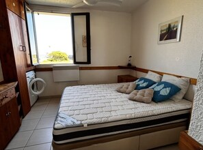 A bedroom with a bed, a washing machine, a radiator, and a window with a view. - Apartment ADA with view - 4 guests (Le Barcarès)