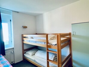 Una camera con un letto a castello, una finestra, una porta e un piccolo ripiano.