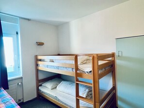 A bunk bed room with a window, a door, and a small cabinet.