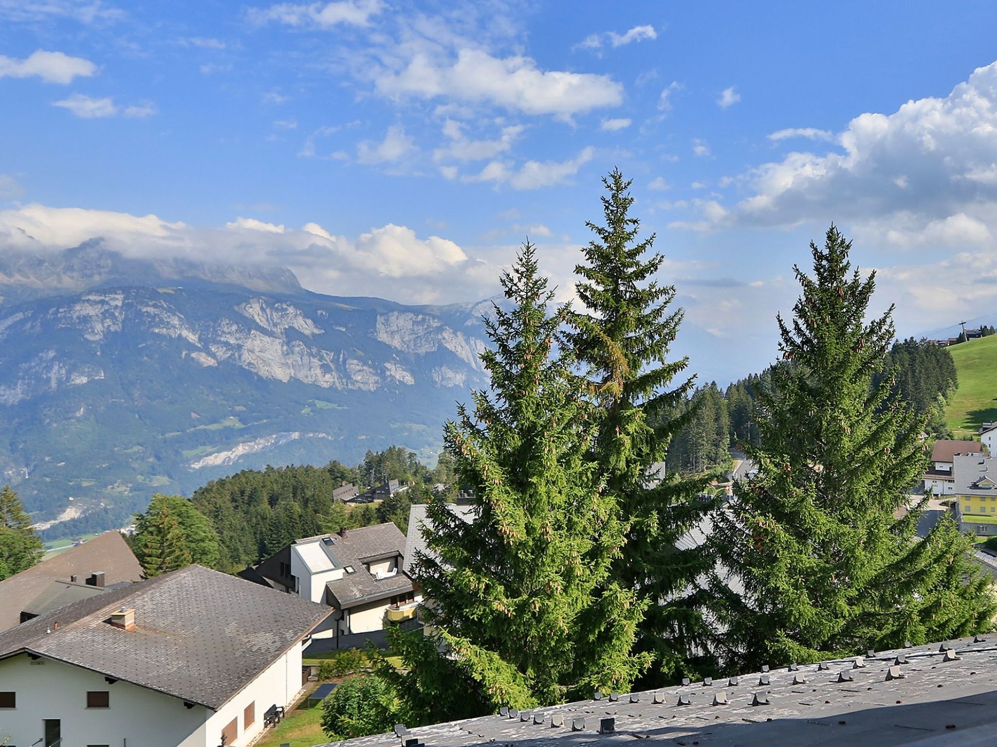 A residential area with houses, a mountain range in the background, and evergreen trees.