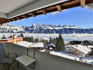 A snow-covered mountain landscape with a view of a chalet-style building and a chair.