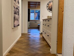 Un couloir avec un plancher en bois, un radiateur, une fenêtre et une horloge fixée au mur.