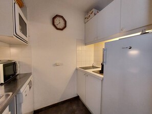 A compact kitchen with white cabinets, a microwave, a clock, and a refrigerator. - Cozy apartment, pets welcome, view of slopes (Valmorel)