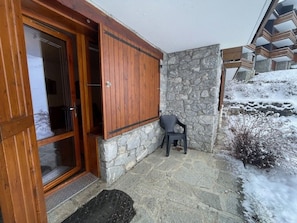 A wooden door with a glass panel, a stone wall, and a small chair outside a building. - Cozy apartment, pets welcome, view of slopes (Valmorel)