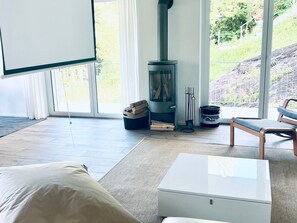 Ein modernes Wohnzimmer mit großem Fenster, eingebautem Holzofen, weißem Couchtisch und einer Bank.