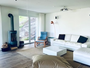Ein modernes Wohnzimmer mit einem weißen Sofa, einem blauen Sessel, einem weißen Couchtisch und einem Kaminofen.