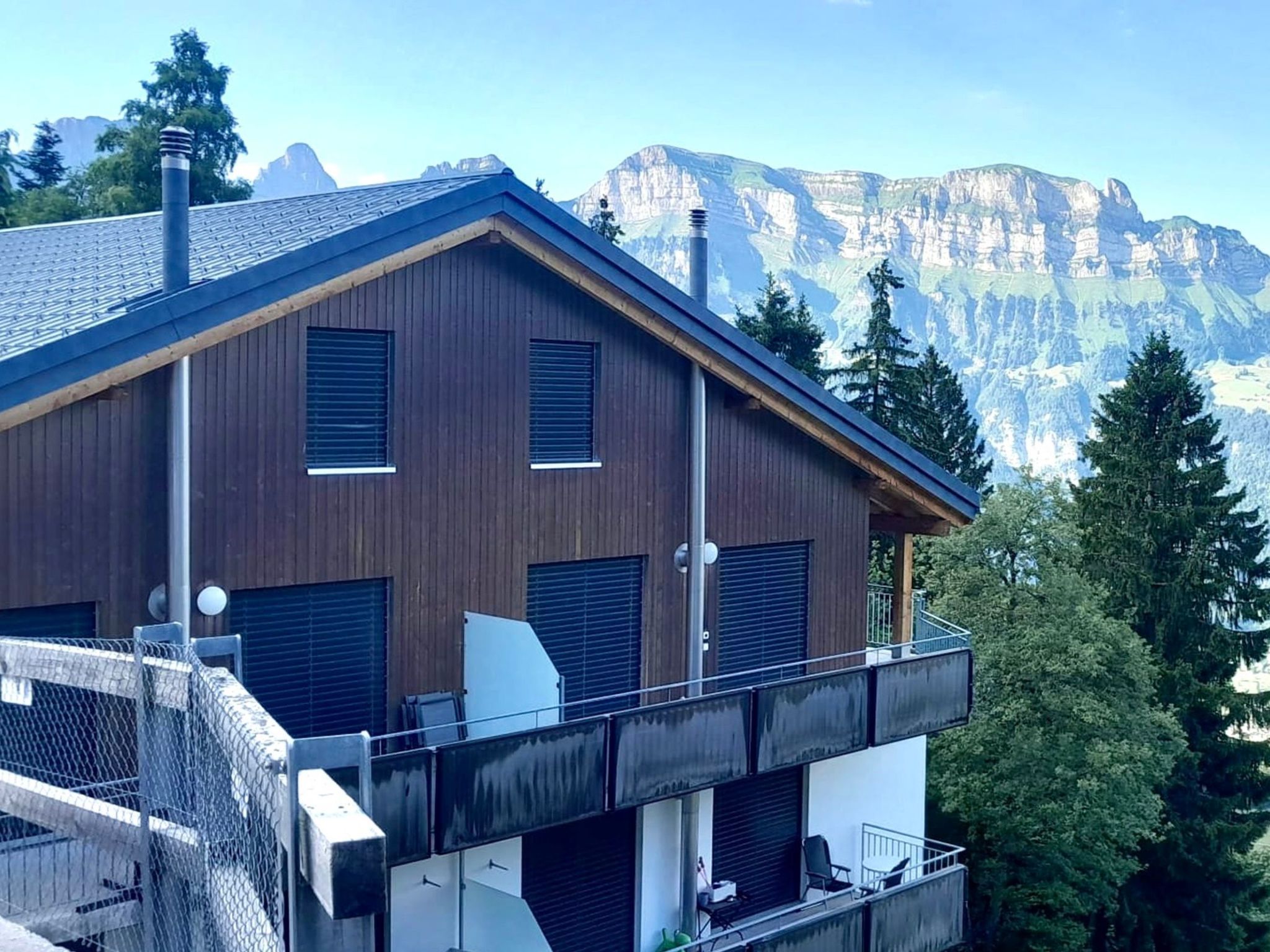 A modern two-story building with a balcony, large windows, and a mountain backdrop.