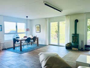 Ein geräumiges Wohnzimmer mit Essbereich, großen Fenstern und einem Kaminofen.
