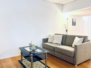 Ein Wohnzimmer mit einem Glastisch, einem grauen Sofa und einer Stehlampe.