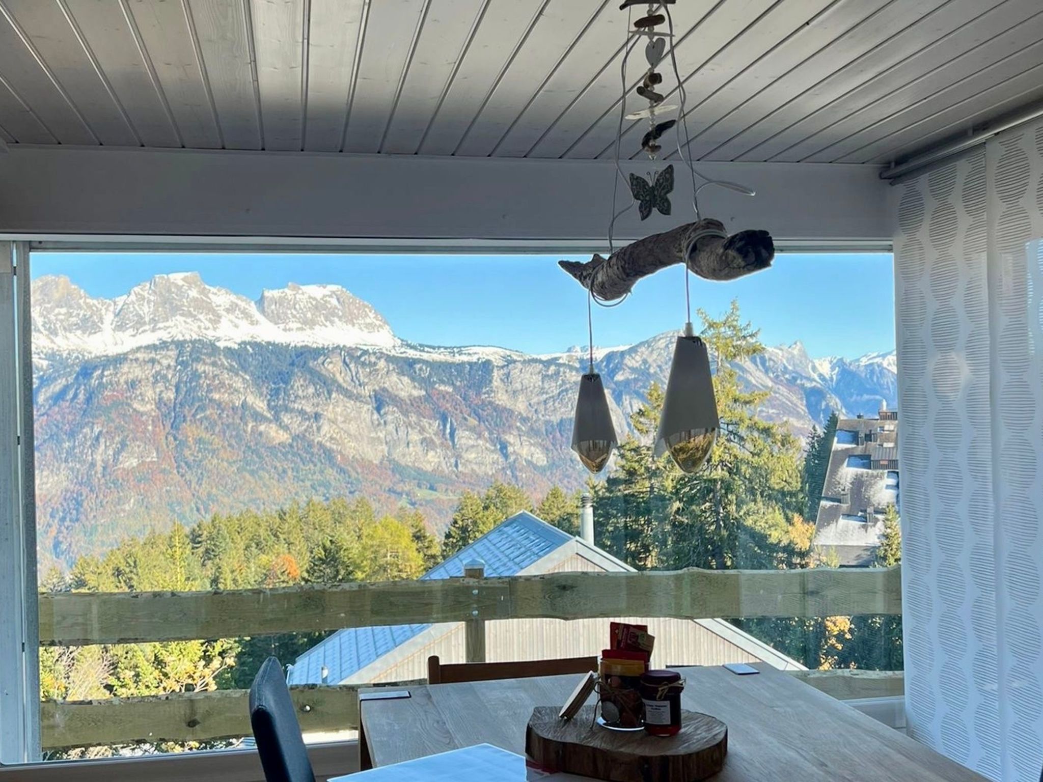 A room with a view of snow-capped mountains, a wooden table with a chair, and a hanging bird sculpture.