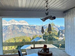 A room with a view of snow-capped mountains, a wooden table with a chair, and a hanging bird sculpture. - Chalet Windegg (CharmingStay), (Flumserberg Tannenheim), by Interhome (Flumserberg Tannenheim)