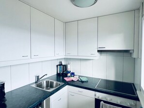 A modern kitchen with white cabinets, a black countertop, stainless steel sink, and a built-in oven. - Chalet Windegg (CharmingStay), (Flumserberg Tannenheim), by Interhome (Flumserberg Tannenheim)