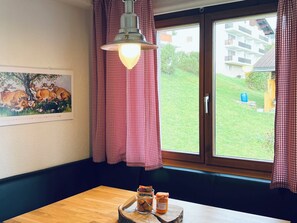 Una stanza con un tavolo in legno, una lampada a sospensione, una finestra con tende a quadri e un quadro appeso al muro.