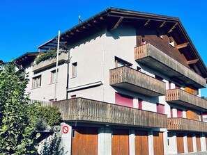 Un edificio a più piani con balconi, un'area parcheggio privata e un cielo azzurro intenso.