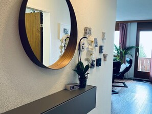 A hallway with a round mirror, a potted plant, and a small shelf with a book.