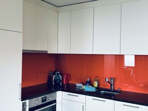 Una cucina moderna con mobili bianchi, una parete di fondo rosso e elettrodomestici in acciaio inossidabile.