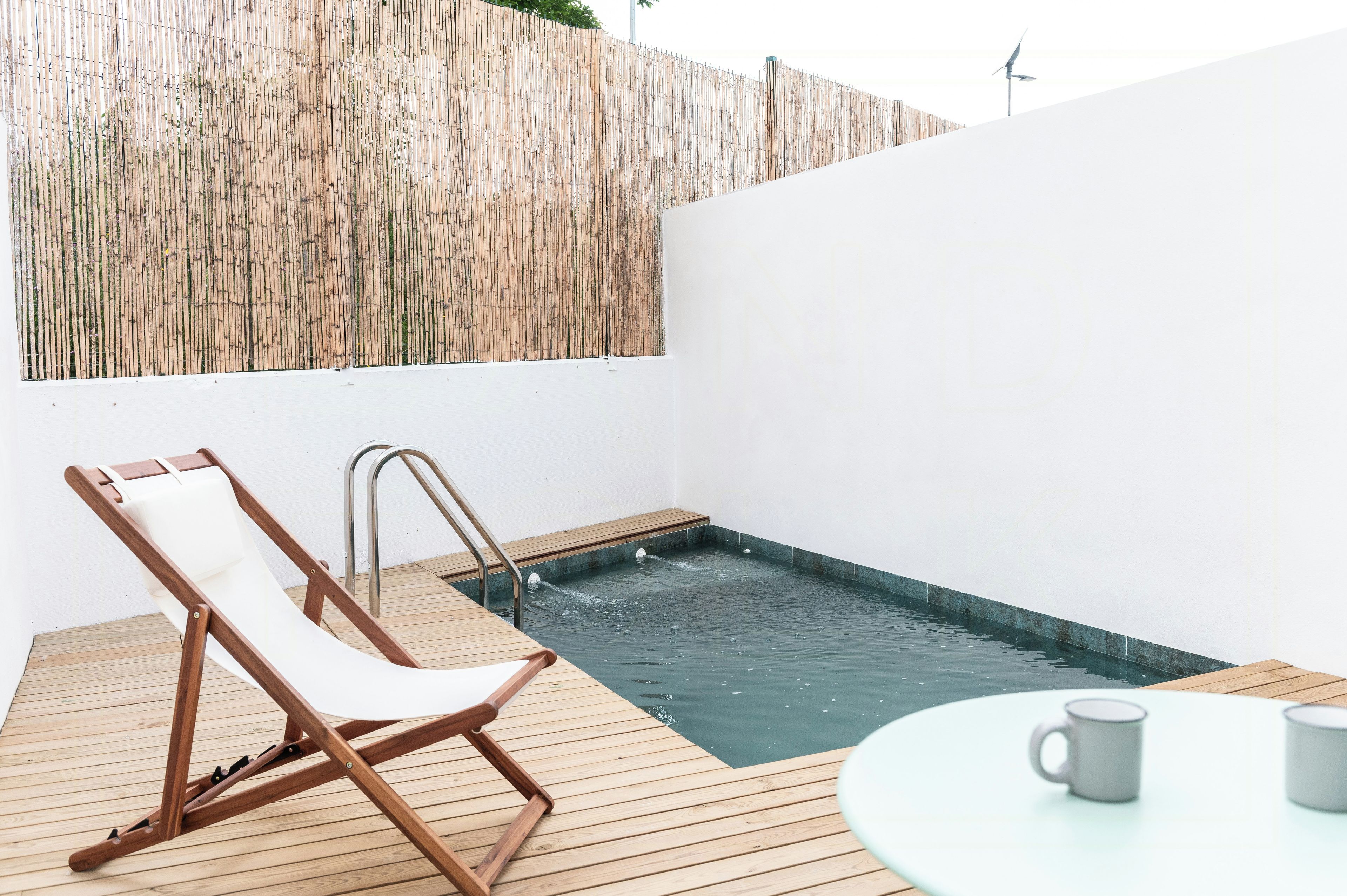Eine Holzterrasse mit Pool, Liegestuhl und Tisch mit zwei Tassen.