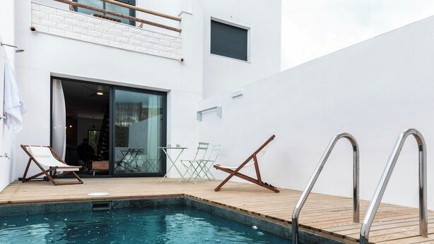 A modern outdoor pool area with a wooden deck, lounge chairs, and a glass door leading to an interior space. - House with a pool, ideal for visiting Andalusia. (Luque)