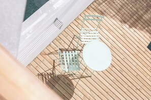 Een houten terras met een ronde tafel en een metalen stoel.