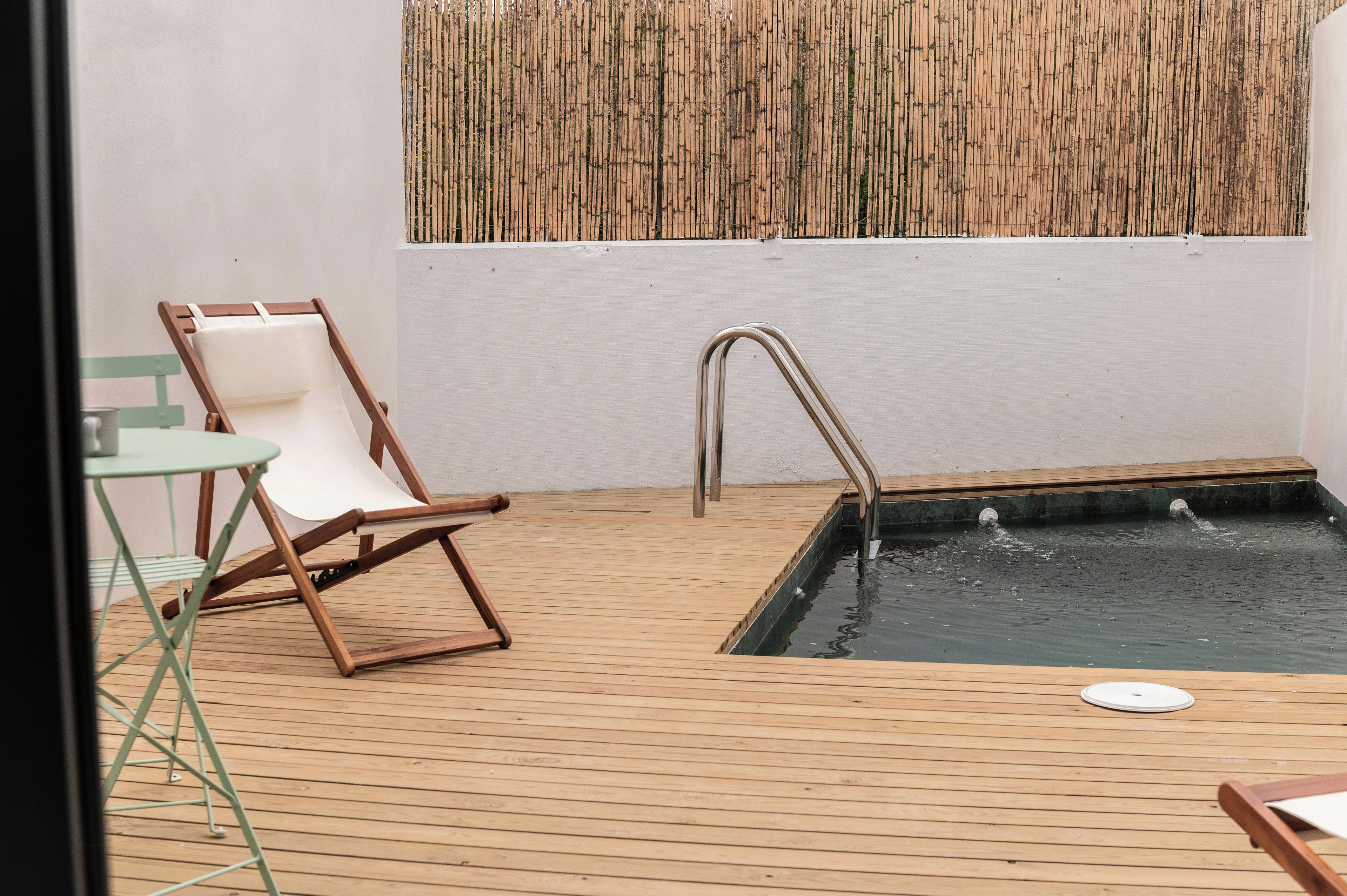 Una terraza de madera con piscina, una silla de descanso y una mesita.
