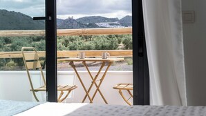 A room with a bed, a wooden chair, a small table with two cups, and a view of a mountainous landscape through an open door. - House with a pool, ideal for visiting Andalusia. (Luque)