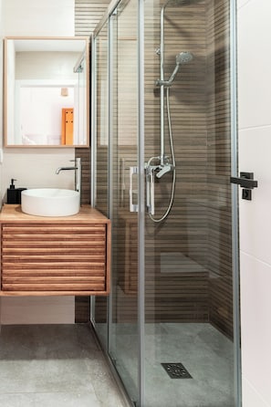 Un baño moderno con ducha envuelta en vidrio, tocador de madera y lavamanos blanco.