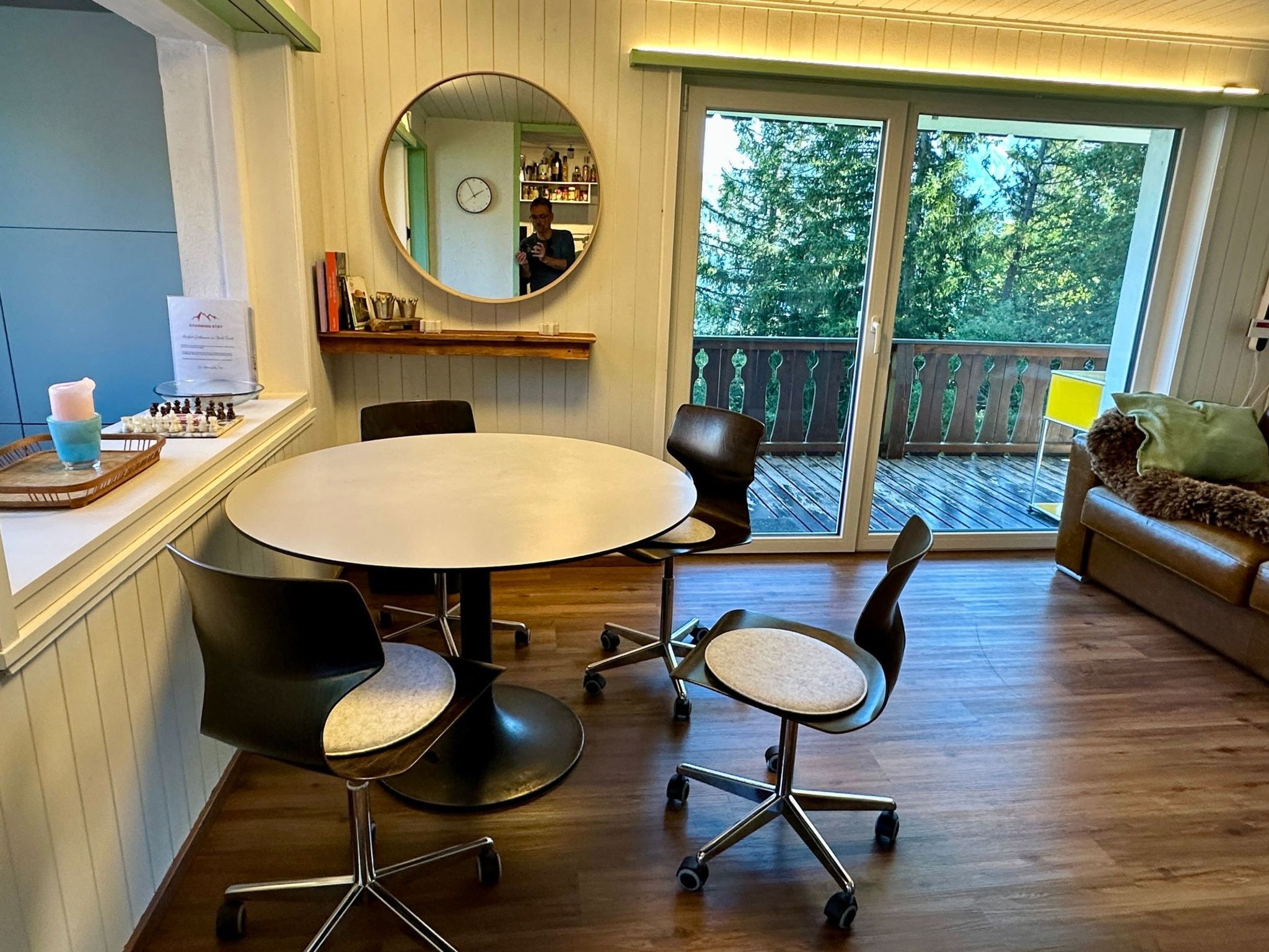 Een eethoek met een ronde tafel, vier stoelen, een spiegel, een klok en uitzicht op het buitenlandschap.