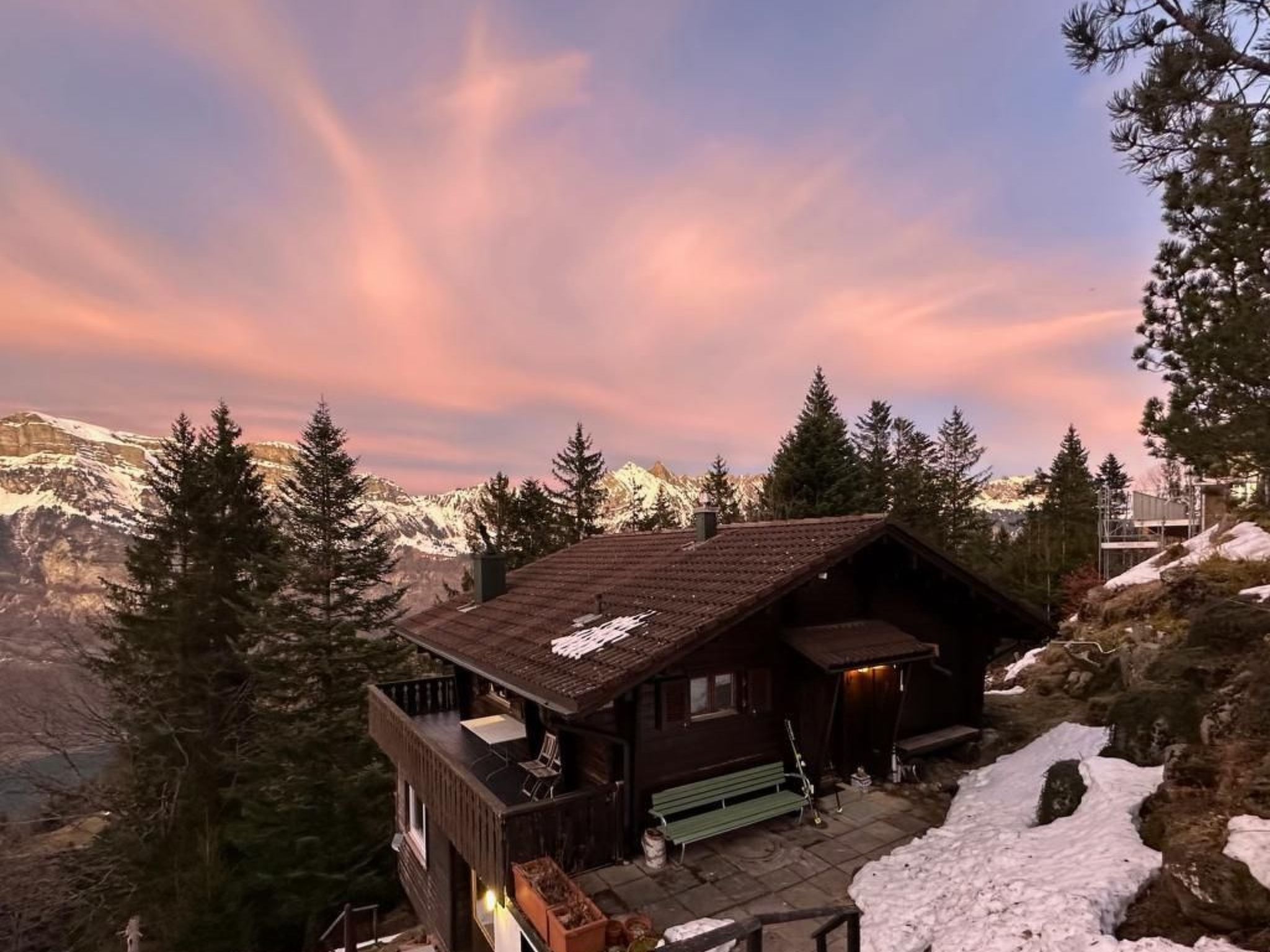 A cabin with a wooden exterior, a porch, and a view of snow-covered mountains.