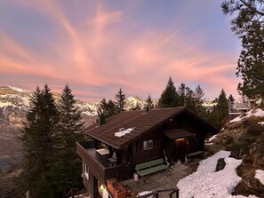 A cabin with a wooden exterior, a porch, and a view of snow-covered mountains. - Chalet Tännli (CharmingStay), (Flumserberg Tannenbodenalp), by Interhome (Flumserberg Tannenbodenalp)