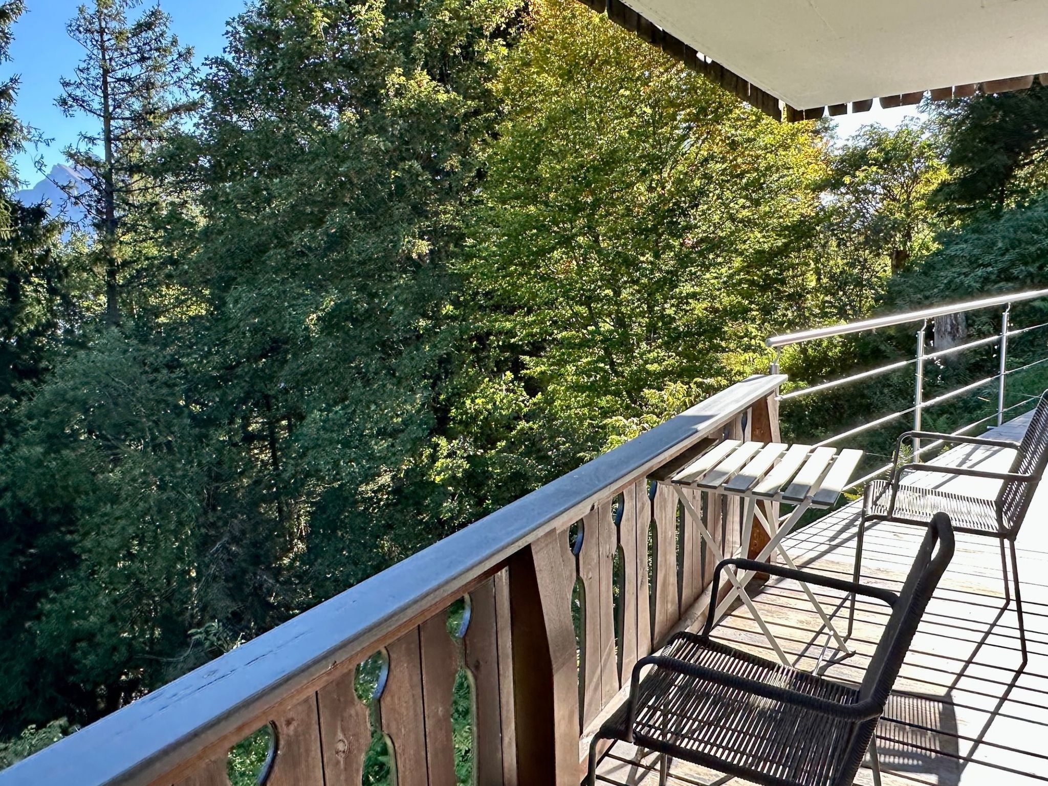 A wooden deck with metal railings overlooking a forested area.