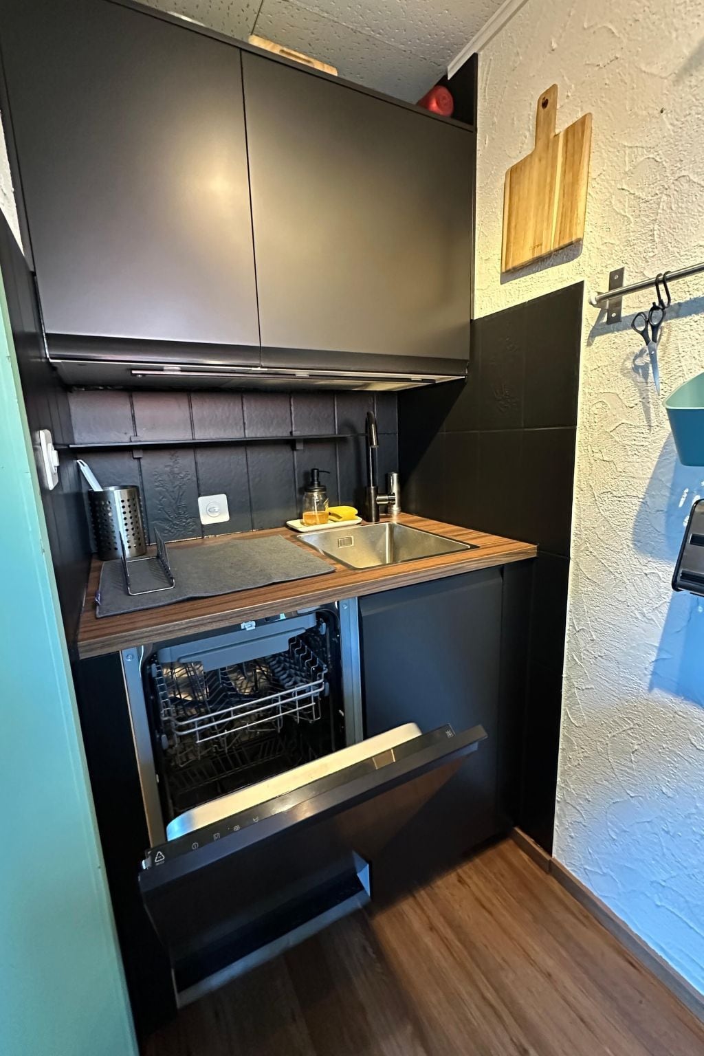 Eine kleine Küche mit integriertem Geschirrspüler, einer Holz Arbeitsplatte und einem schwarzen Küchenschrank.