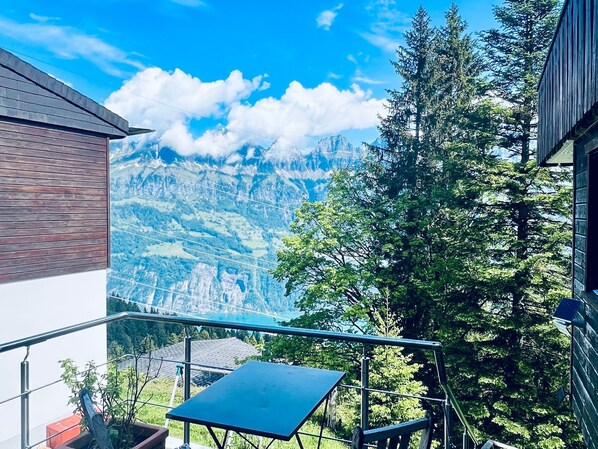 A balcony with a table and chairs, overlooking a mountainous landscape with trees and a clear sky. - Chalet Tännli (CharmingStay), (Flumserberg Tannenbodenalp), by Interhome (Flumserberg Tannenbodenalp)