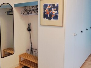 Ein Zimmer mit einem Spiegel, einem gerahmten abstrakten Gemälde, einem Kleiderständer und einer hölzernen Bank.