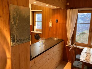 A small kitchen with wooden walls, a window with a view, and a table with chairs. - Chalet Schwendihus (CharmingStay), (Flumserberg Tannenbodenalp), by Interhome (Mols)