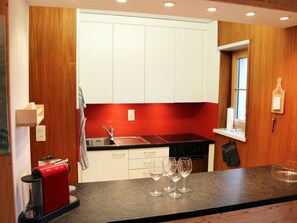 A compact kitchen with white cabinets, a red countertop, a sink, and a stove. - Chalet Schwendihus (CharmingStay), (Flumserberg Tannenbodenalp), by Interhome (Mols)
