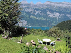 A grassy outdoor area with a table and chairs, overlooking a lake and mountains. - Chalet Schwendihus (CharmingStay), (Flumserberg Tannenbodenalp), by Interhome (Mols)