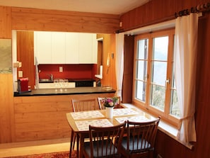 A wooden interior with a kitchen, dining area, and a window with curtains. - Chalet Schwendihus (CharmingStay), (Flumserberg Tannenbodenalp), by Interhome (Mols)