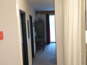 A hallway with a door on the left, a cabinet with bottles on top, and a chair in the center. - Haus Wogesa (CharmingStay), (Flumserberg Tannenboden), by Interhome (Flumserberg Tannenheim)