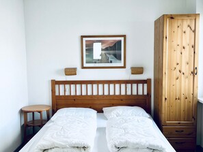 Una cama doble con cabecera de madera, una mesita redonda pequeña, un armario y un cuadro enmarcado en la pared.