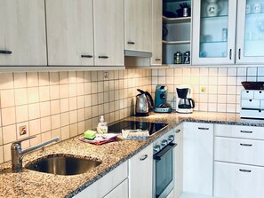 A kitchen with white cabinets, a granite countertop, a coffee maker, a kettle, and a sink. - Haus Wogesa (CharmingStay), (Flumserberg Tannenboden), by Interhome (Flumserberg Tannenheim)