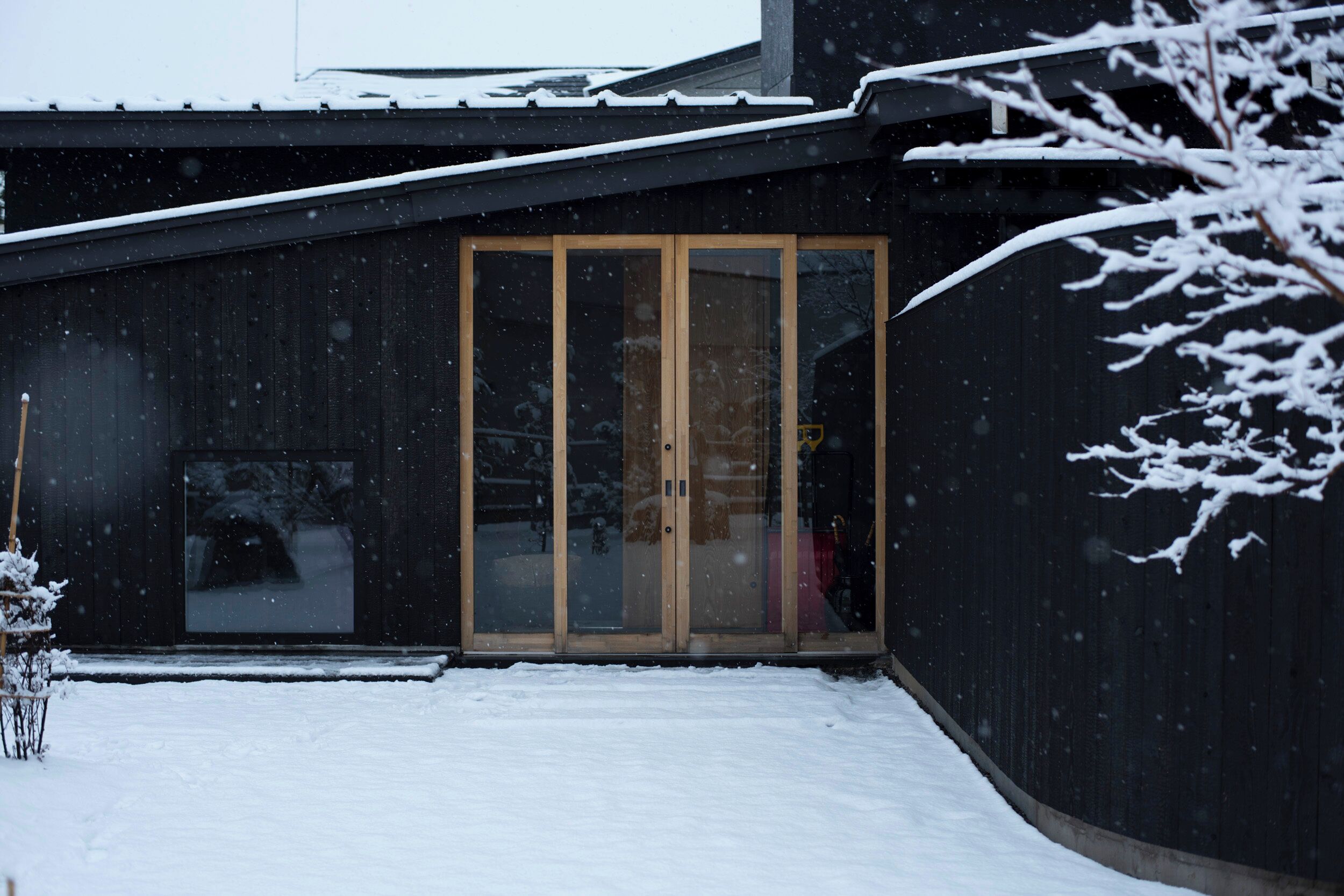 Ein modernes Gebäude mit dunkler Fassade, einer Holztür und einem mit Schnee bedeckten Dach.