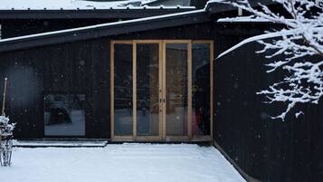 Ein modernes Gebäude mit dunkler Fassade, einer Holztür und einem mit Schnee bedeckten Dach.