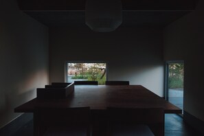 Ein moderner Essbereich mit einem langen Tisch, Stühlen, einer Hängelampe und Blick auf einen Garten durch ein Fenster.