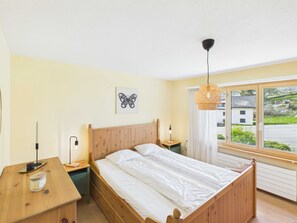 A bedroom with a wooden bed, bedside tables, a lamp, a window with a view, and a wall-mounted light fixture.