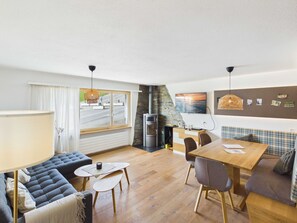 A modern living room with a sofa, dining table, and chairs, a fireplace, and a view through a large window.